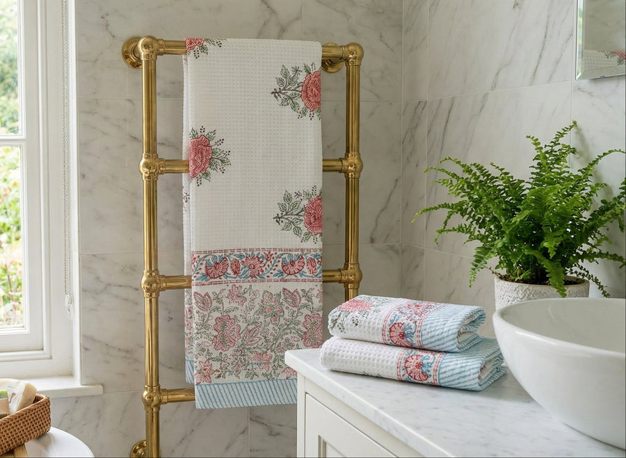 Bathroom with floral towels on a gold towel rack, window, and plant.