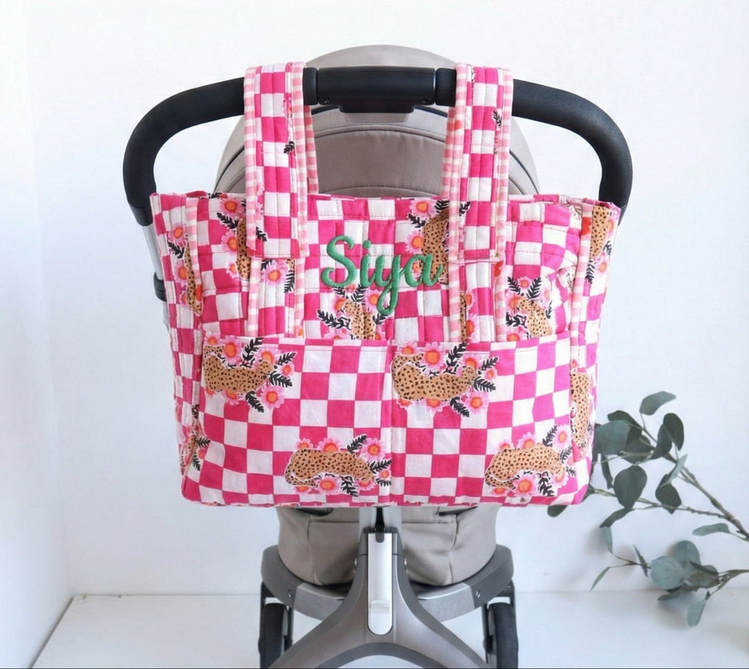 Pink checkered bag with embroidered name on a stroller handle against a white background